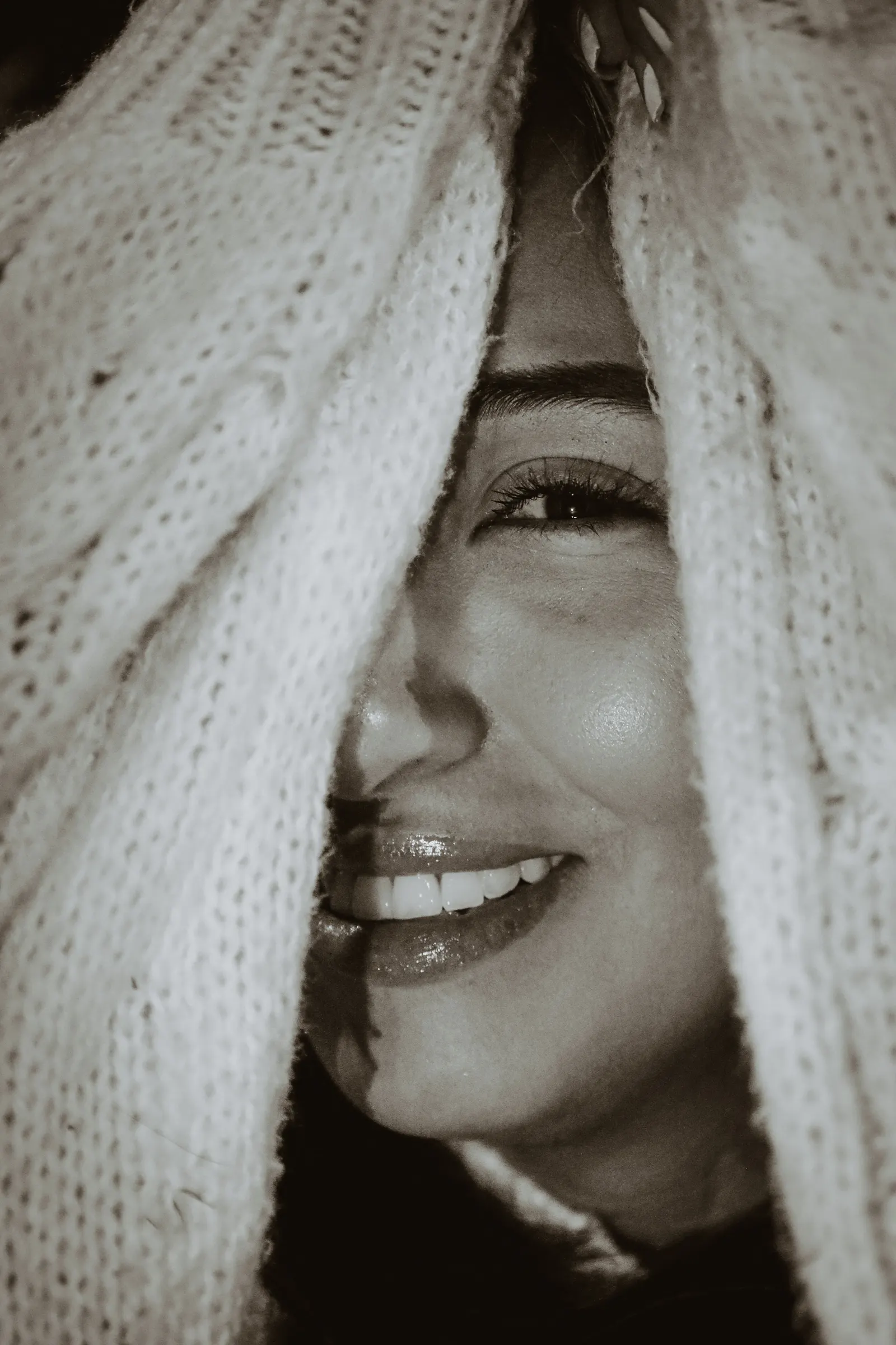 A woman smiling warmly from under a cream knit sweater